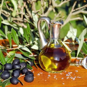 Olio extra vergine di oliva in una brocca di vetro poggiata su un tavolo di legno con olive nere e fronde di ulivo